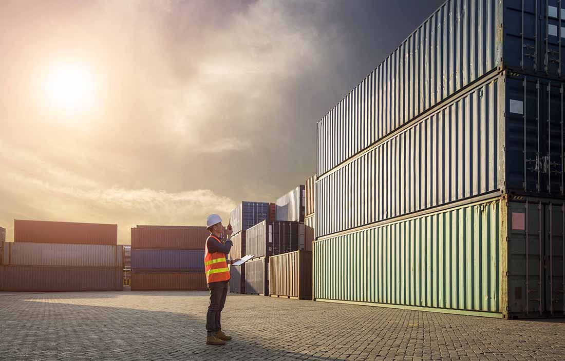 Worker standing outside looking at shipping crates and talking on a radio