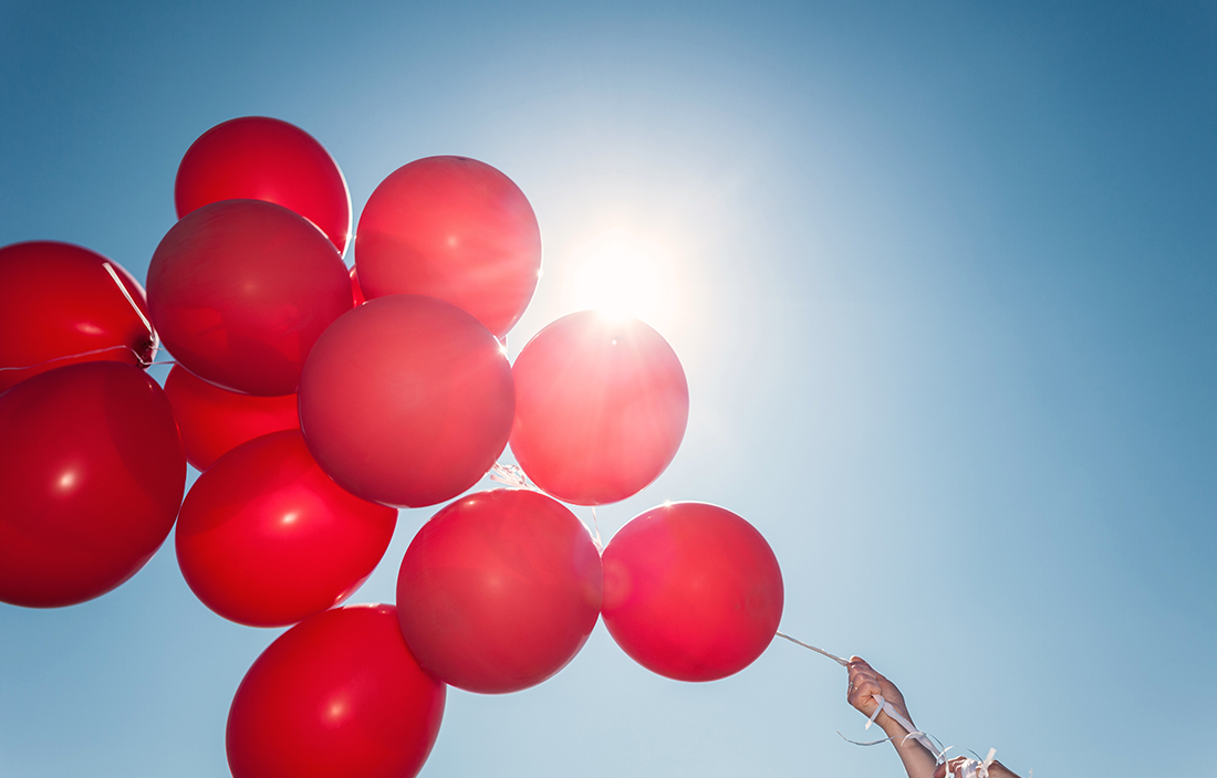Close-up photo of red balloons with a view of the sky in the background.