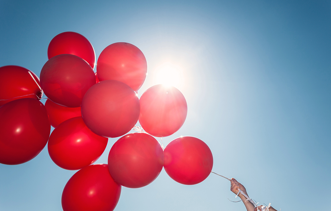Close-up photo of red balloons with a view of the sky in the background.