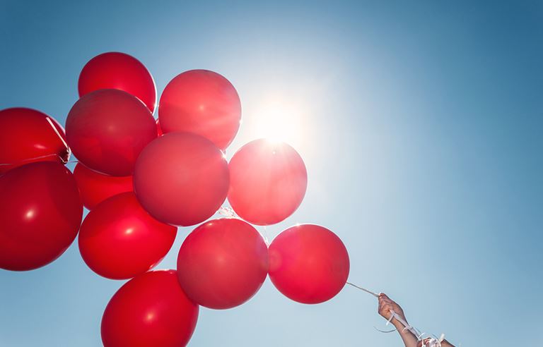 Close-up photo of red balloons with a view of the sky in the background.