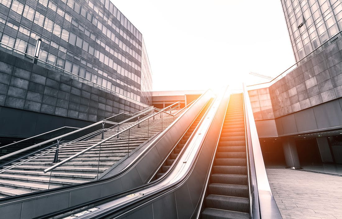 View of an escalator in a downtown area with a sunrise in the background.