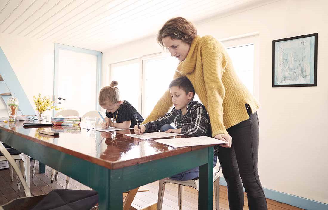 A parent with their children watching them draw with colored pencils at the table.