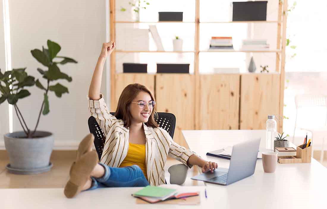 Business professional celebrating with a hand raised in the air while using a laptop computer.