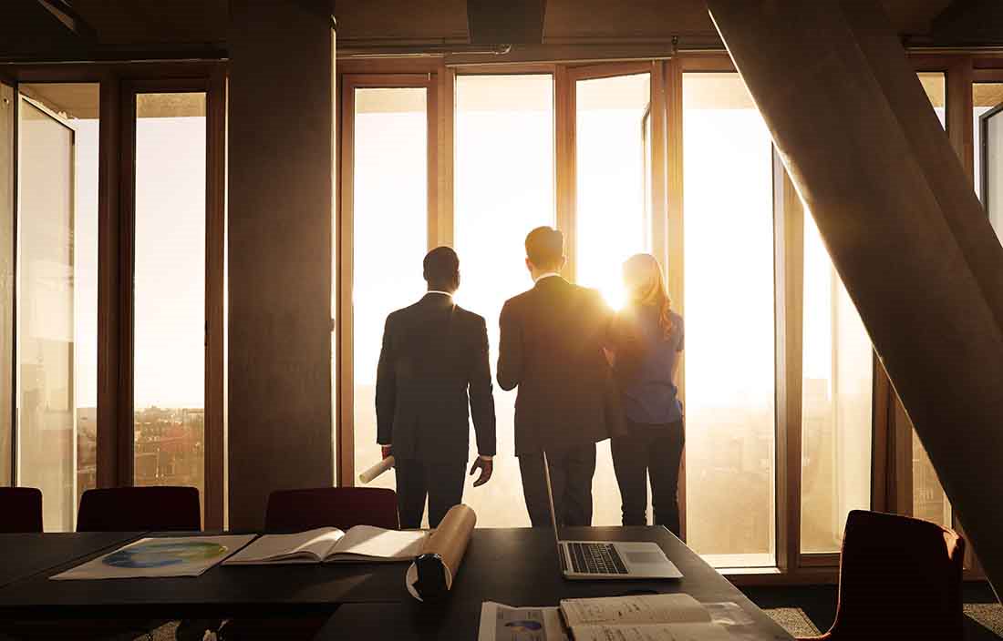 Business professionals looking out a window during sunrise.