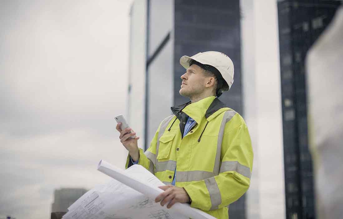Construction worker holding documents in one hand while looking into the sky.