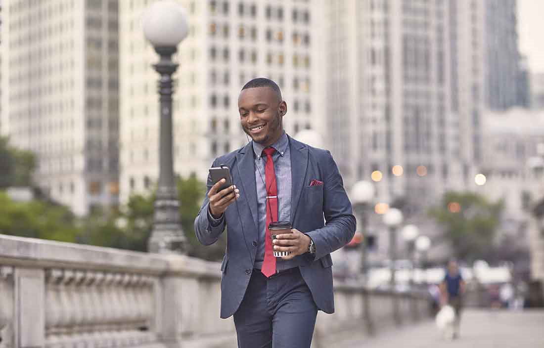 Business professional walking on a bridge while checking their cell phone.