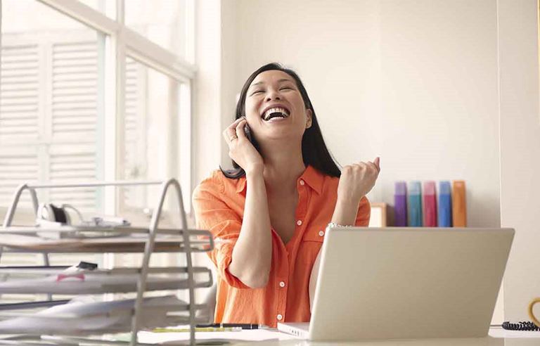 Business professional celebrating with their hands in the air while taking a phone call.