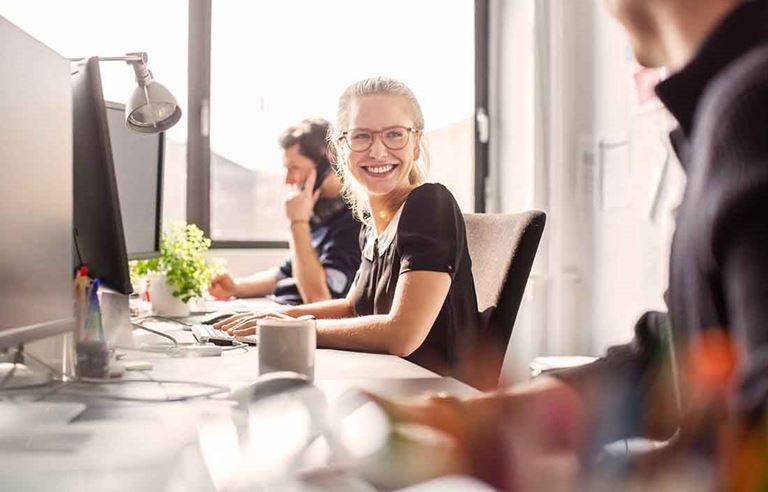 Business professionals sitting at their cubicle desks smiling at each other.