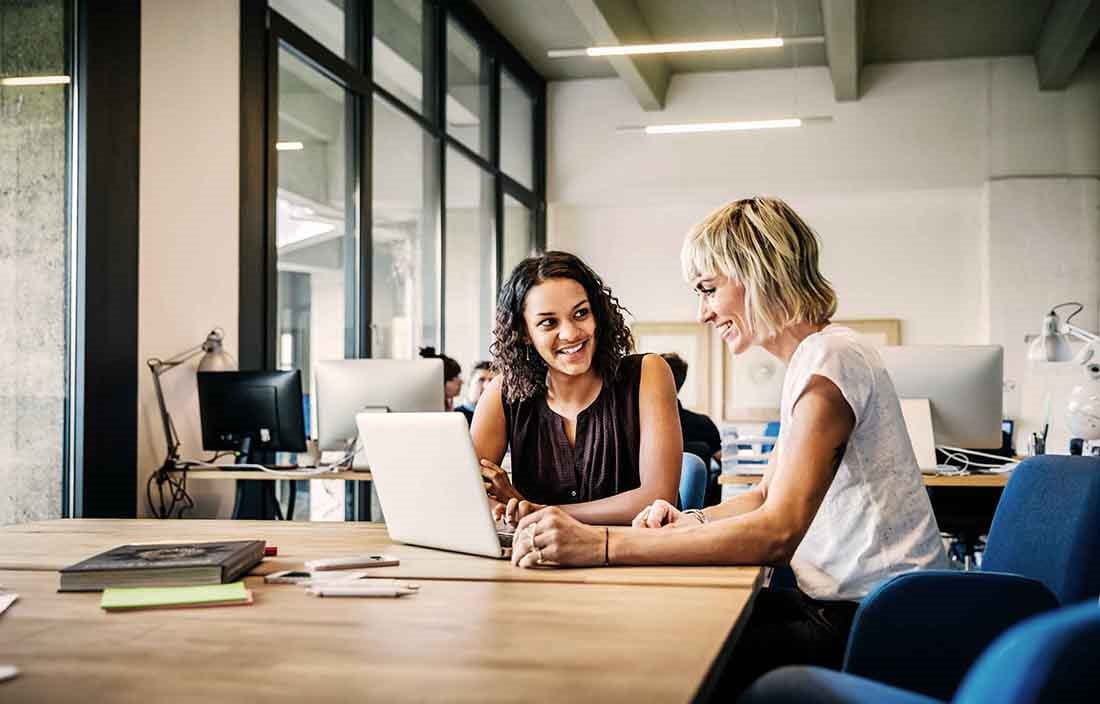 Two business professionals sitting at a table looking at a laptop together.