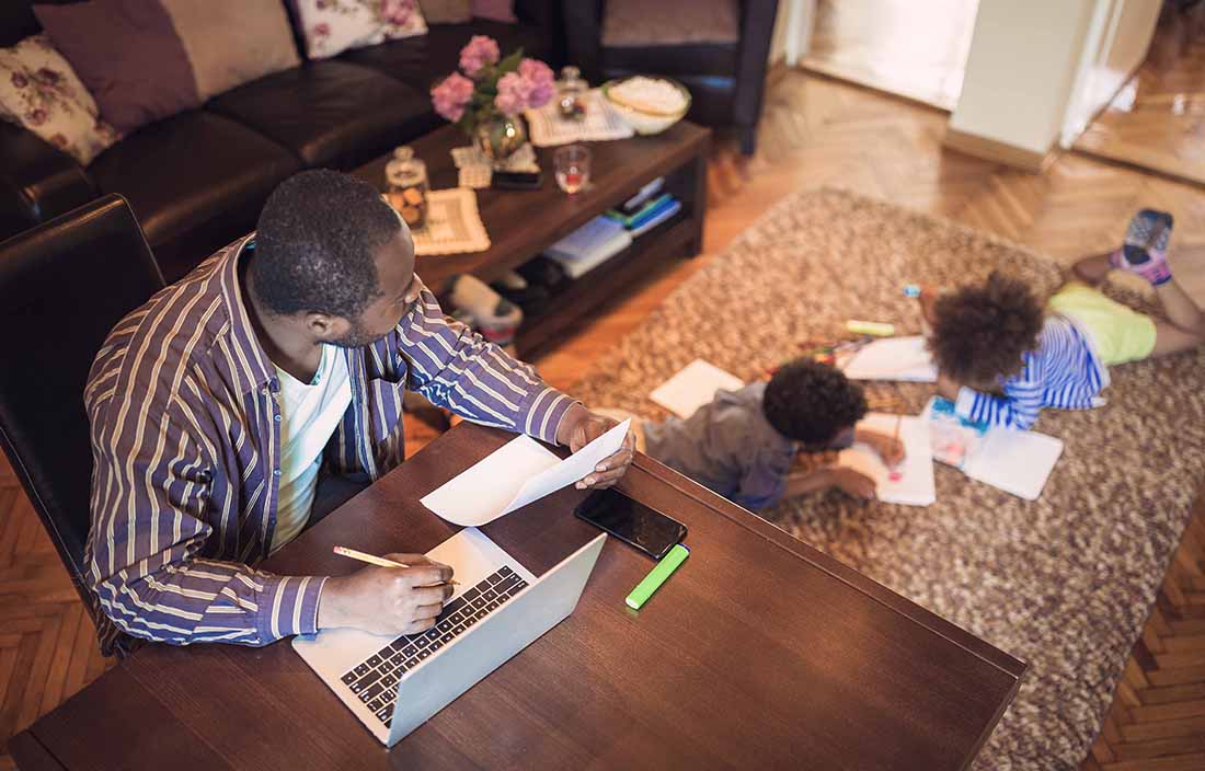 Parent using their laptop computer while a child plays on the floor nearby. 