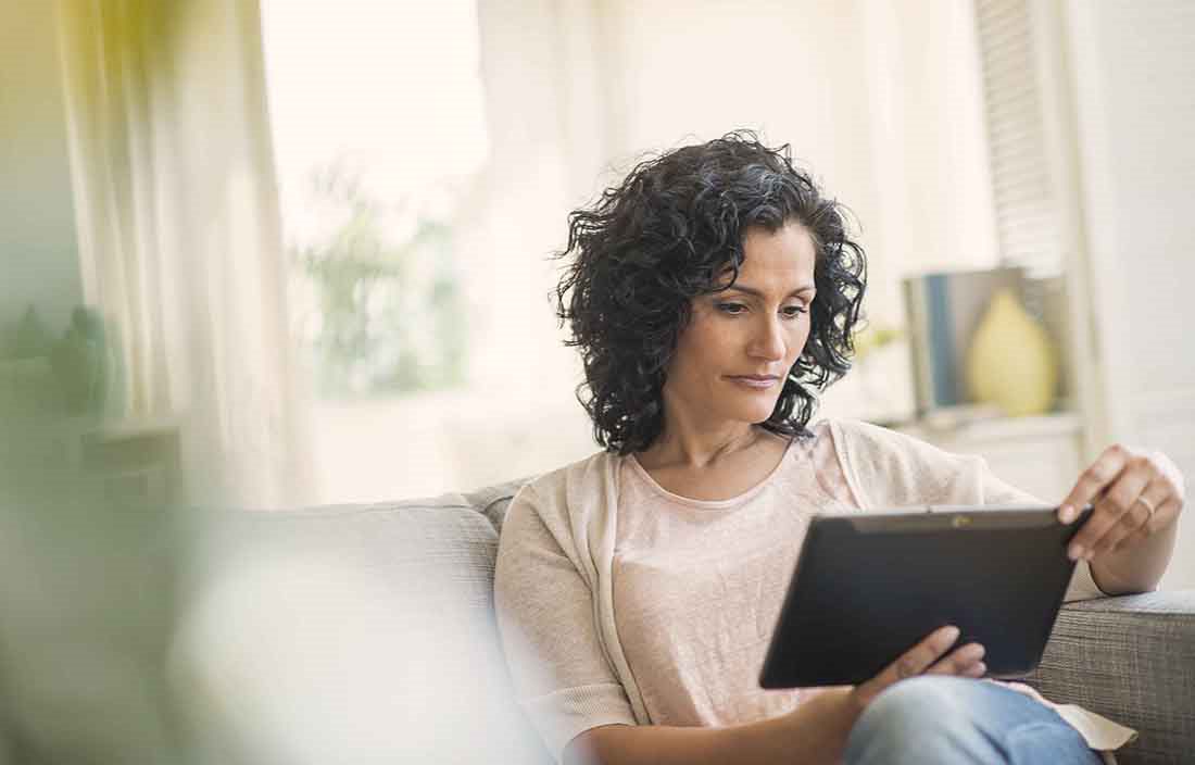 Woman in casual clothes at home sitting on a couch using a tablet device.