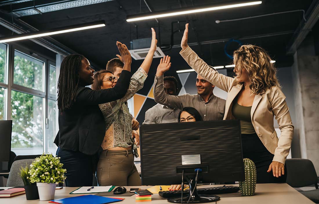 A group of business professionals celebrating and giving each other high-fives in the office.