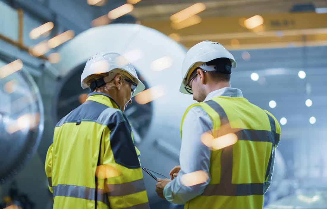 Workers in safety vest in a factory floor setting.