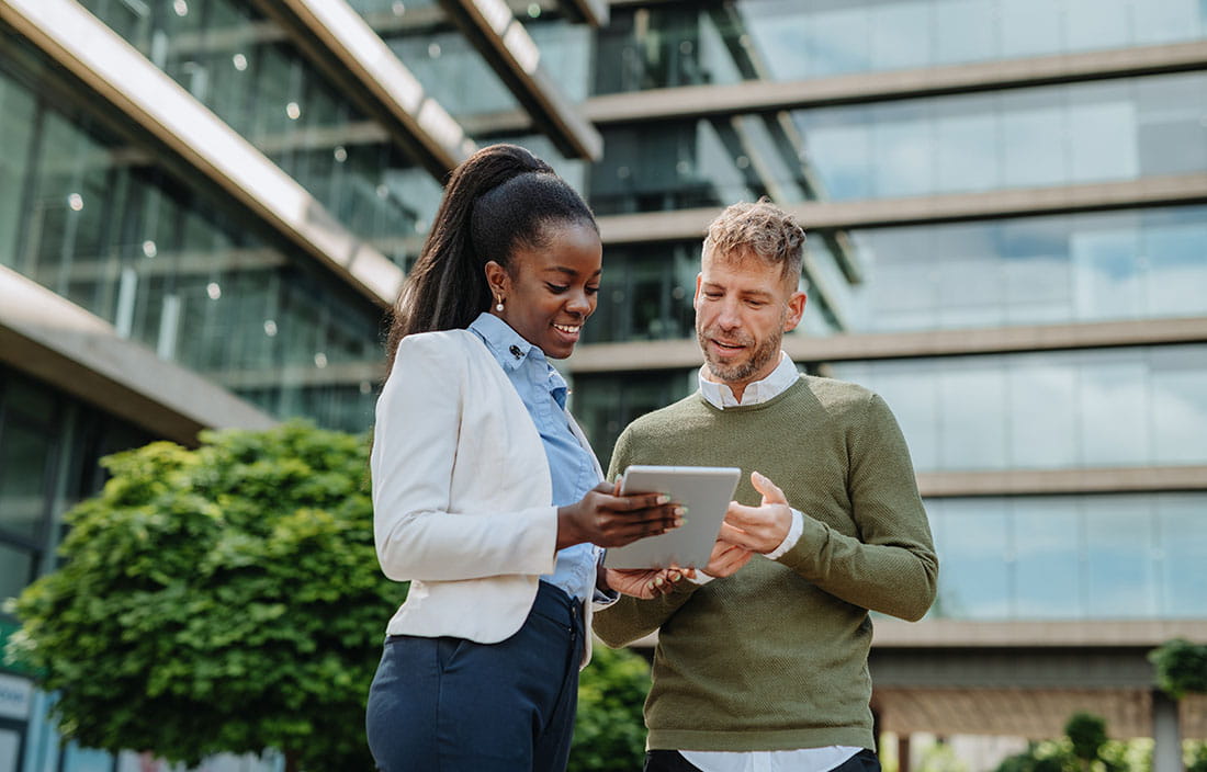 Two people looking at tablet computer outside of an office building.