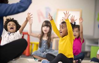 Kids in a class raising their hands. 