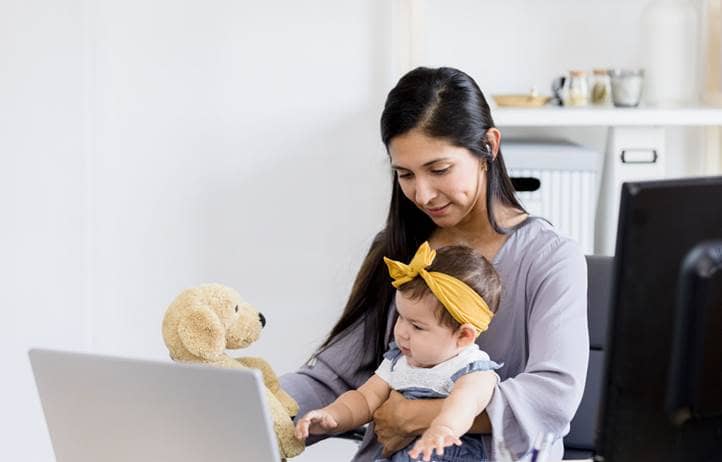Woman working on her laptop with a baby in her lap.