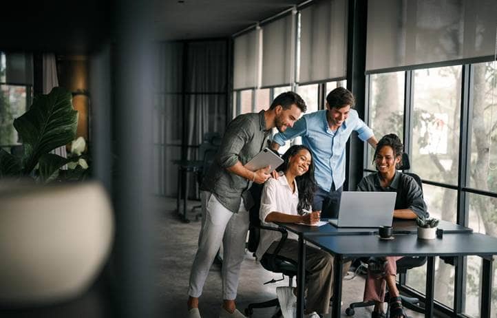 Group of coworkers gathered around a laptop.