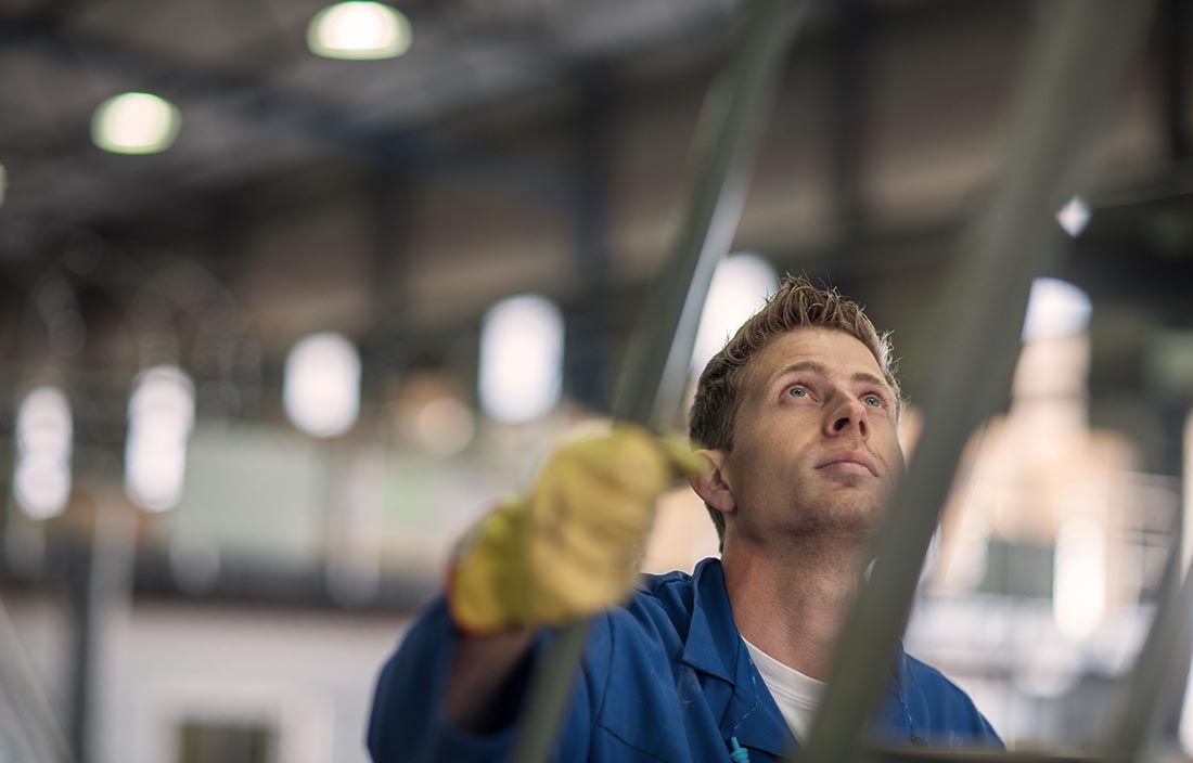 Close up image of a factory worker in truck manufacturing plant, wearing gloves and a jumpsuit, climbing up a set of metal stairs or platform