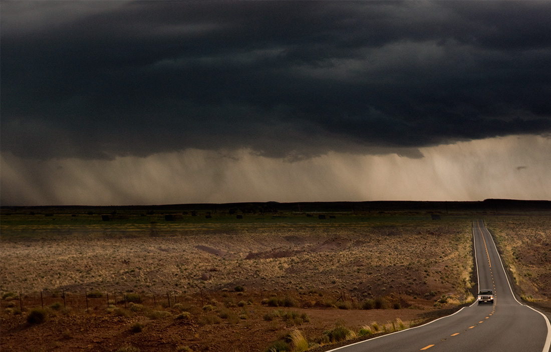 Image of car driving on a desert road heading away from a storm