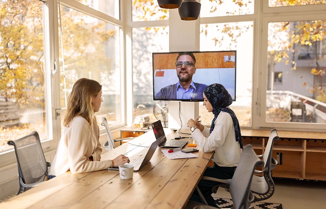 Two professionals in a conference room holding a video call with someone working remote