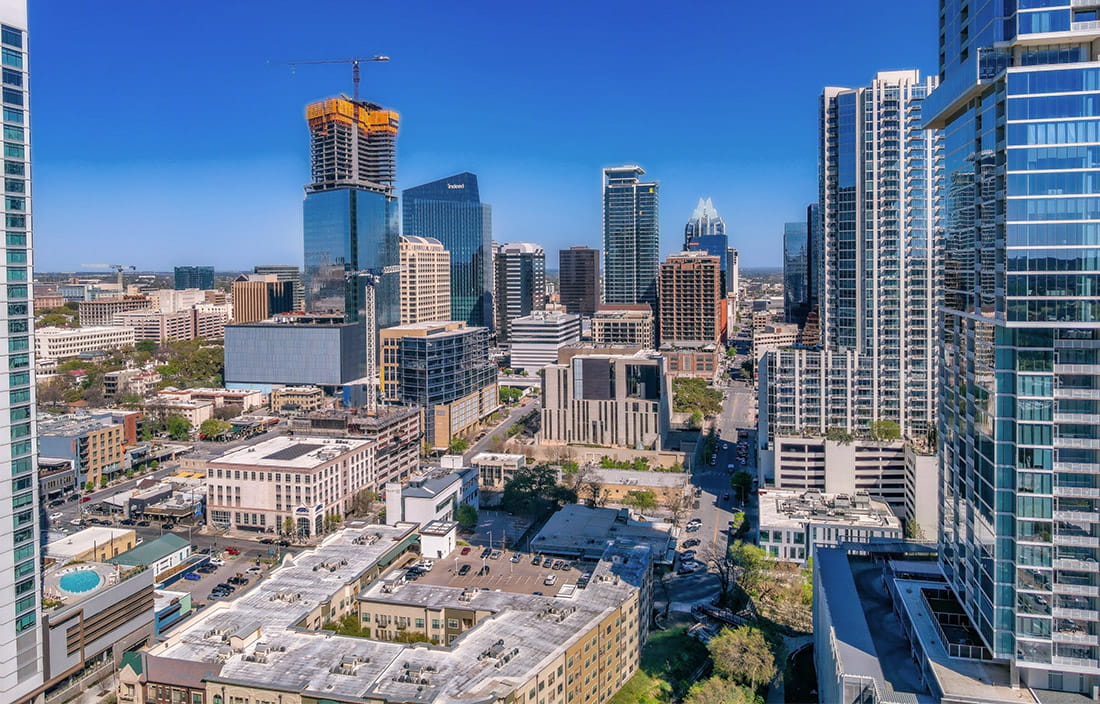 Aerial view of an urban city, with a variety of skyscraper and smaller office buildings, including one in the distance under construction