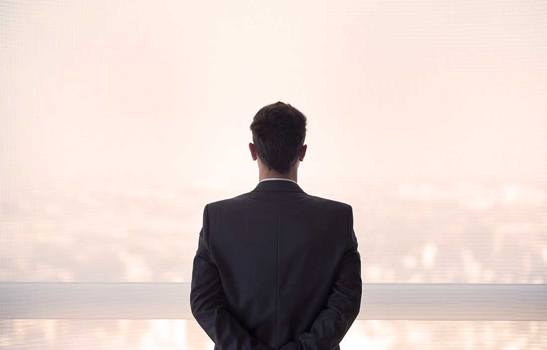 Executive, male and fairly young, looking out a window over real estate with his back toward the viewer