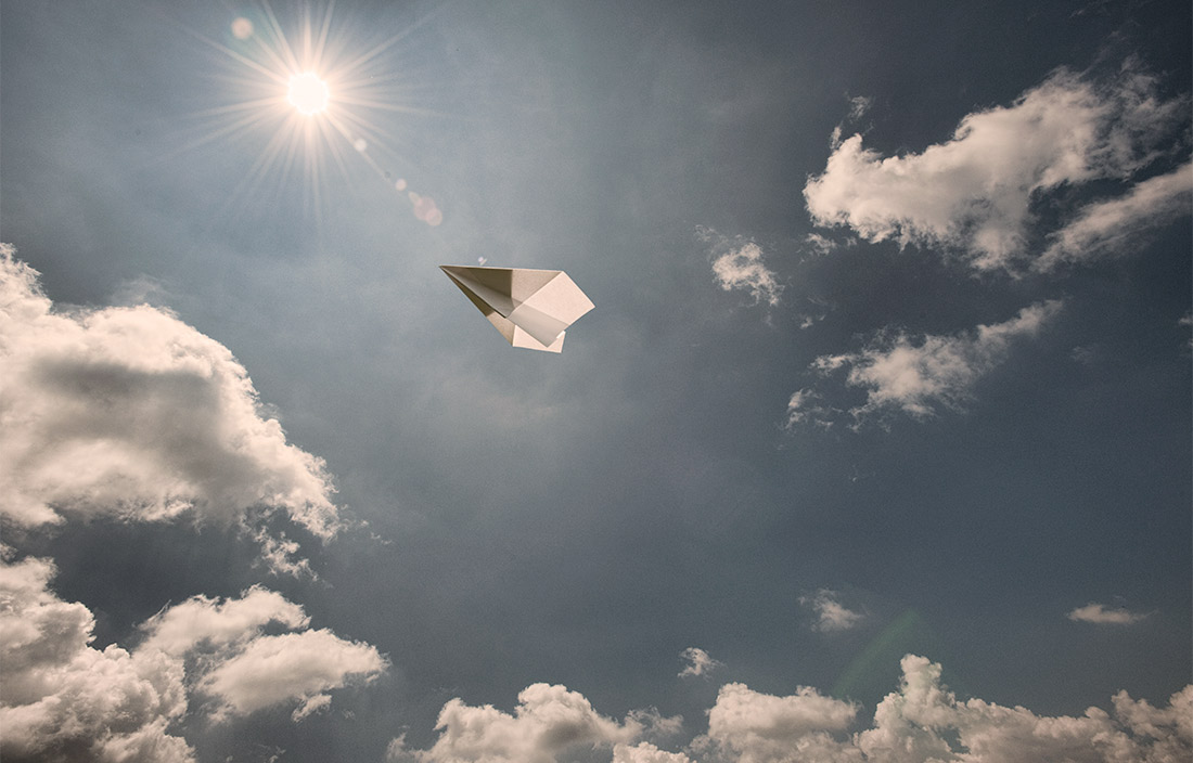 paper airplane flying high in a sunny sky