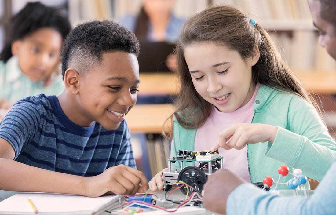 Two kids learning about a robotics project from a teacher