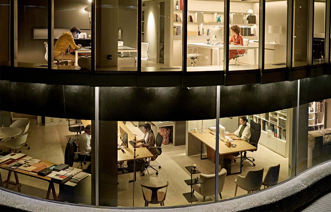 Looking into an ofice building at night to see people working at desks