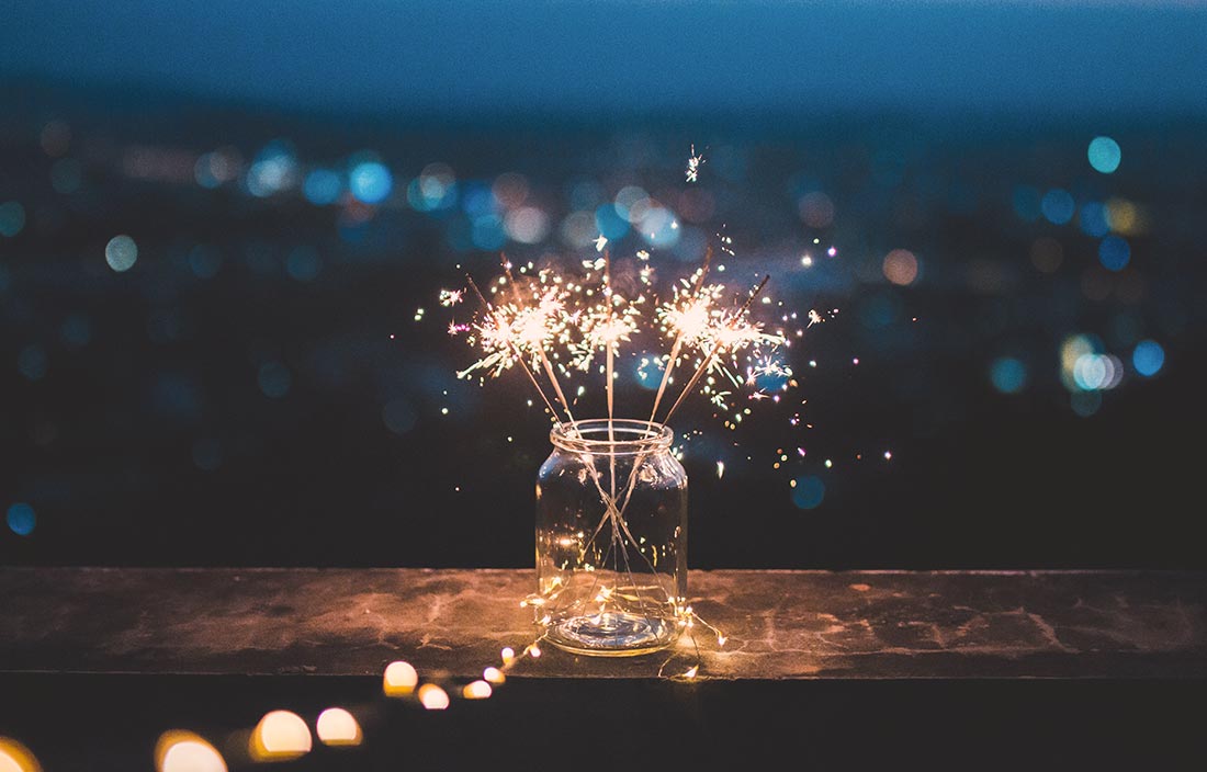Sparklers in a mason jar on the ledge of a wooden porch at night