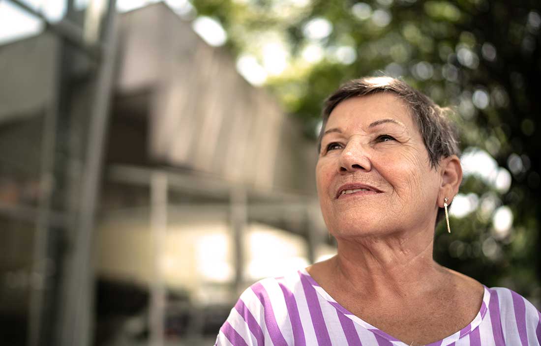 Senior woman outdoors in front of a new senior living housing unit looking up and away toward the left