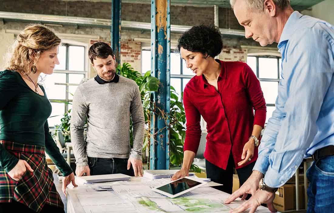 Senior living development team of four, men and women, around a table with construction documents and a tablet discussing a project