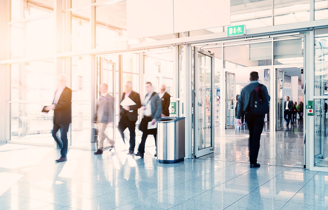 Crowd of anonymous businesspeople walking into and out of a modern hall or hotel for a conference