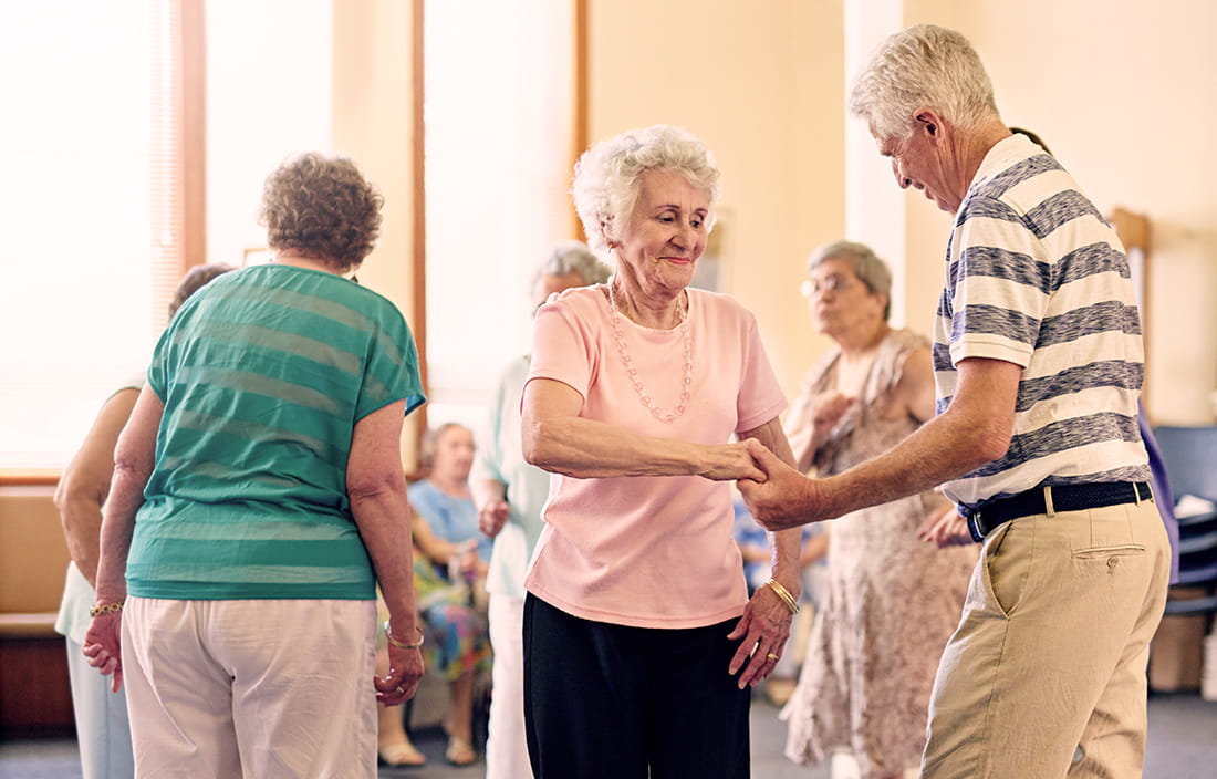 Seniors at an adult day care center dancing in a large, well-lit room
