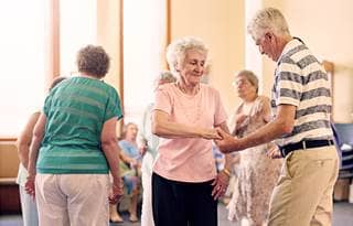 Seniors at an adult day care center dancing in a large, well-lit room