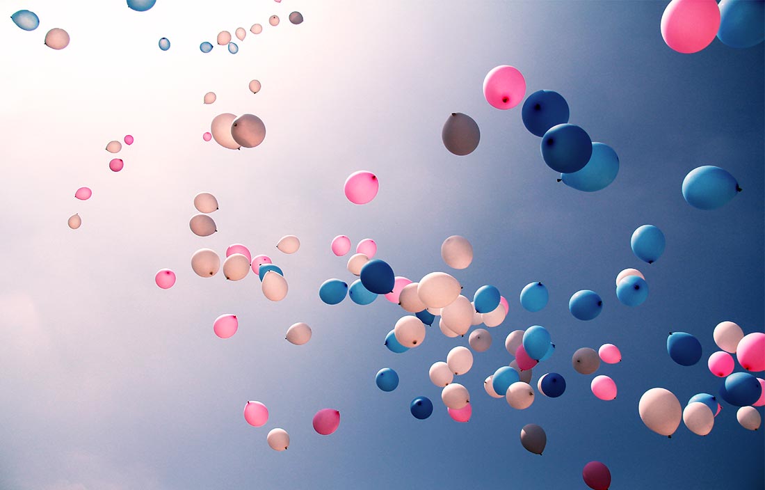 Pink and blue balloons floating up into a clear blue sky