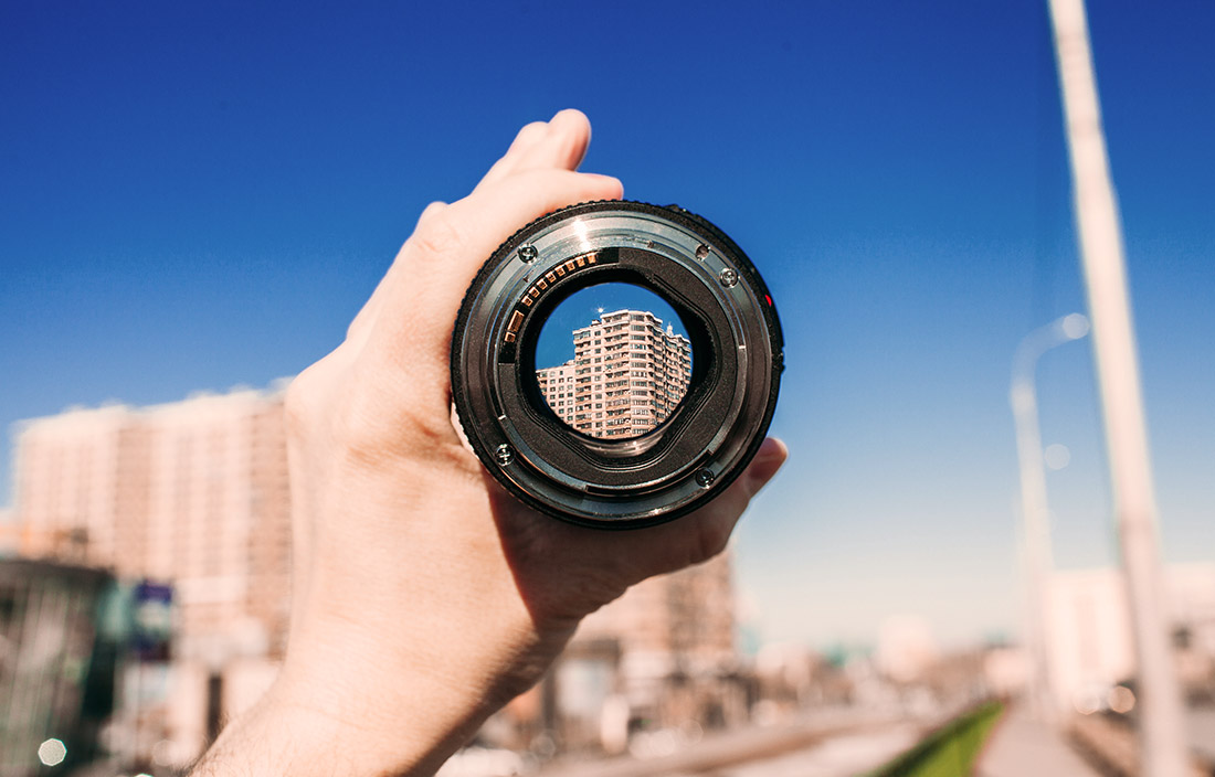 hand holding a lens in front of a blurry city building and road where through the lens a building can be seen clearly