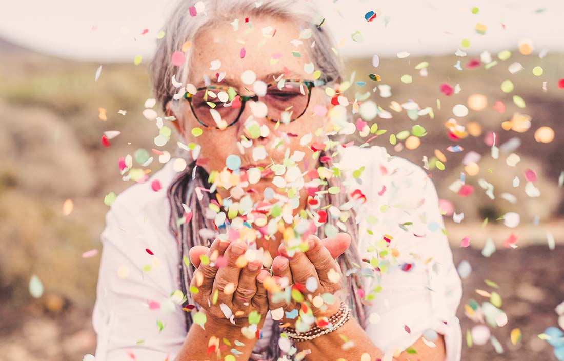 Senior woman blowing confetti to show excitement for new construction on senior living campus