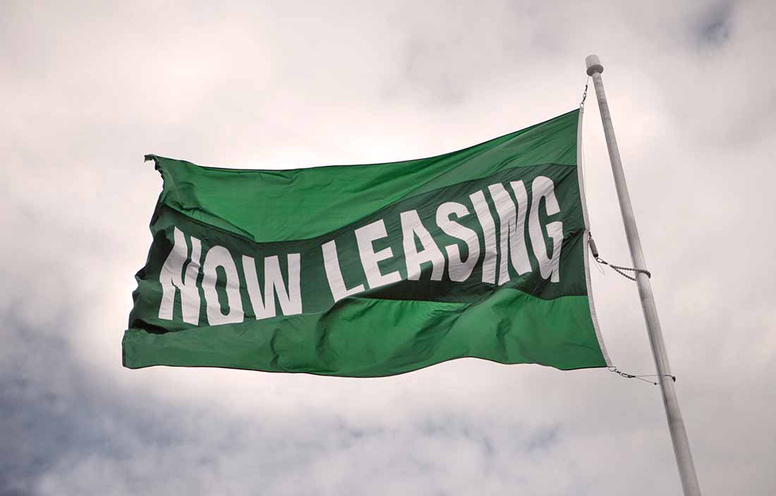 Green flag that says "now leasing" against a cloudy sky for senior housing