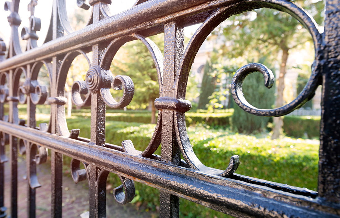 Close up of an iron fence blocking the scene of a building with bushes in front