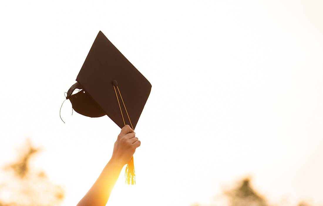 Hand holding up a graduation cap into the air with an abstract, brightly lit background