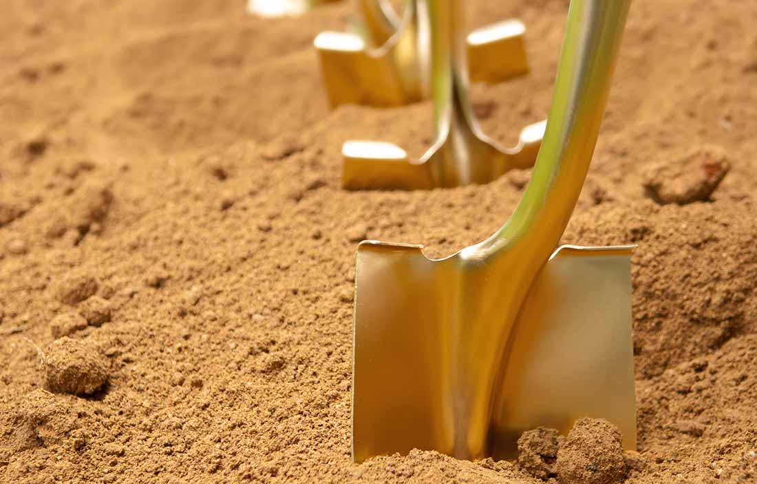 Gold shovels stuck in the dirt in preparation of a groundbreaking ceremony at a senior living construction project