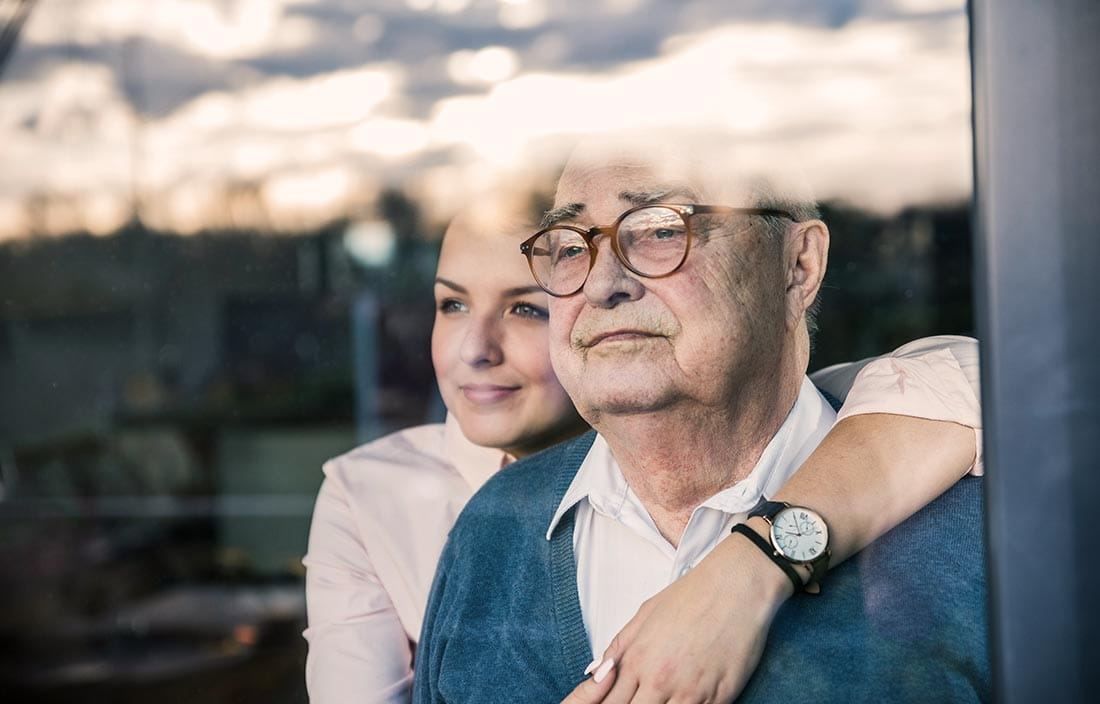 Senior and adult daughter worrying about affording senior living while looking out a window together
