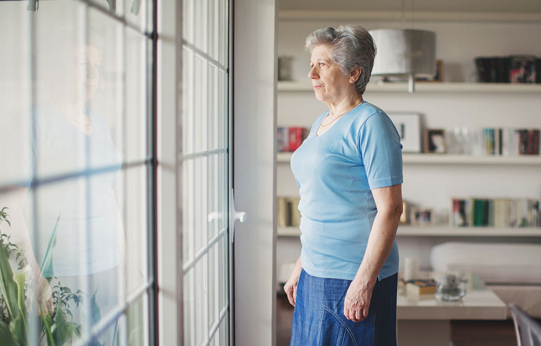 Senior woman looking out the window of her home, concerned
