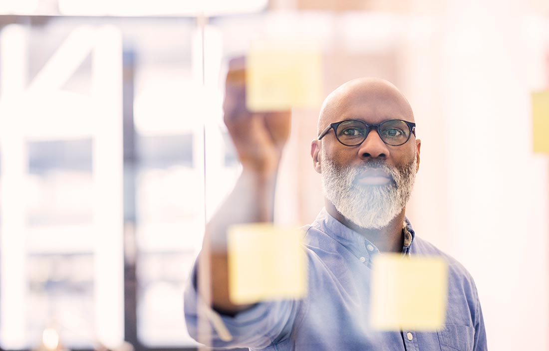 Portrait of businessman taking adhesive note from glass wall in office