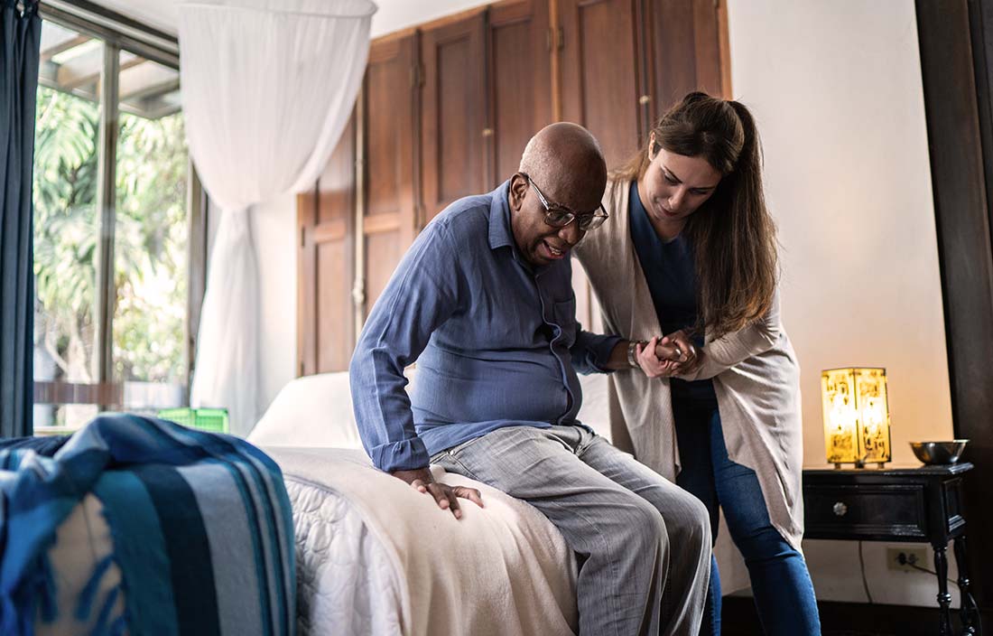 Registered nurse assisting senior out of a bed at a skilled nursing facility