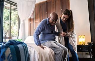 Registered nurse assisting senior out of a bed at a skilled nursing facility