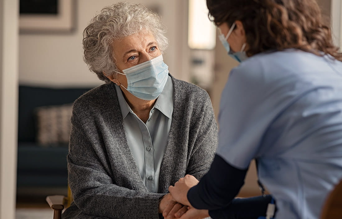 Senior in a skilled nursing facility speaking to a nurse, holding hands