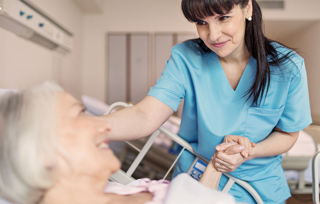 Nurse holding the hand of a senior patient in a hospital bed