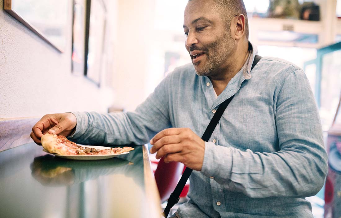 Senior man eats pizza at a restaurant that partners with senior living communities